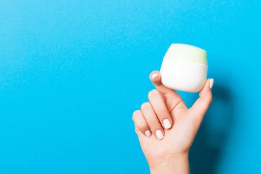 Mavi zemin üzerinde fotokopi alanı olan bir kavanoz kozmetik ürünü tutan kadın elini kapat.