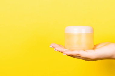 Kadın eli kozmetik kavanozunu sarı arkaplanda tutuyor ve tasarımınız için boş bir alan var..