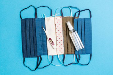 El yapımı pamuk maskeler, alkol el dezenfektanı ve mavi arka planda fotokopi alanı olan dijital termometre. Koruyucu tıbbi ekipman kavramı.