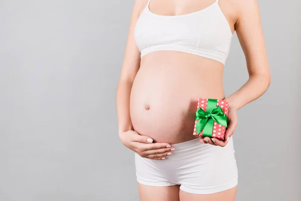 Beyaz Çamaşırlı Hamile Kadının Elinde Gri Arka Planda Bir Hediye — Stok fotoğraf