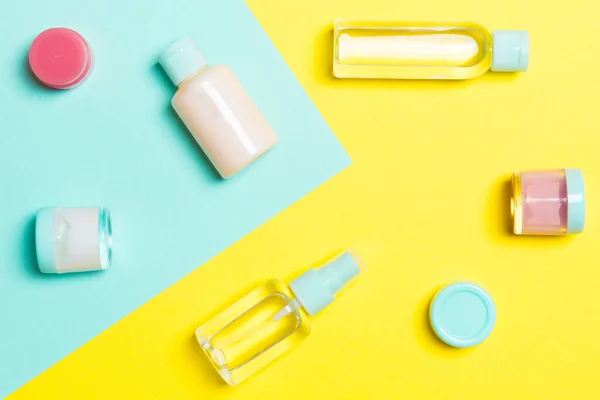 Top view of cosmetic containers, sprays, jars and bottles on yellow and blue background. Close-up view with empty space for your design.
