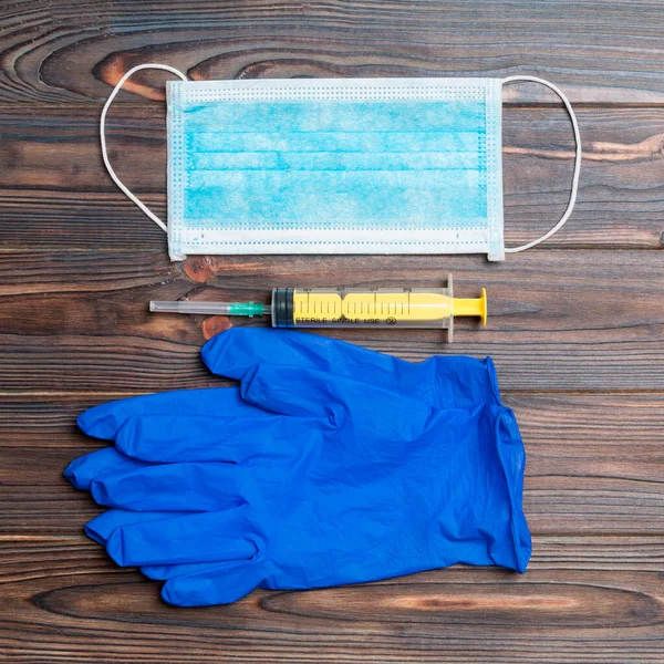 Top view of disposable surgical mask, pair of latex medical gloves and syringe on wooden background. Virus protection concept with copy space.