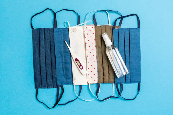 El yapımı pamuk maskeler, alkol el dezenfektanı ve mavi arka planda fotokopi alanı olan dijital termometre. Koruyucu tıbbi ekipman kavramı.