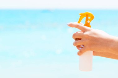 Denizin arka planında elinde güneş kremi tutan bir kadın resmi var..