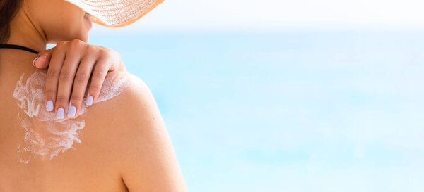 Sunscreen sunblock. Woman in a hat putting solar cream on shoulder outdoors under sunshine on beautiful summer day.
