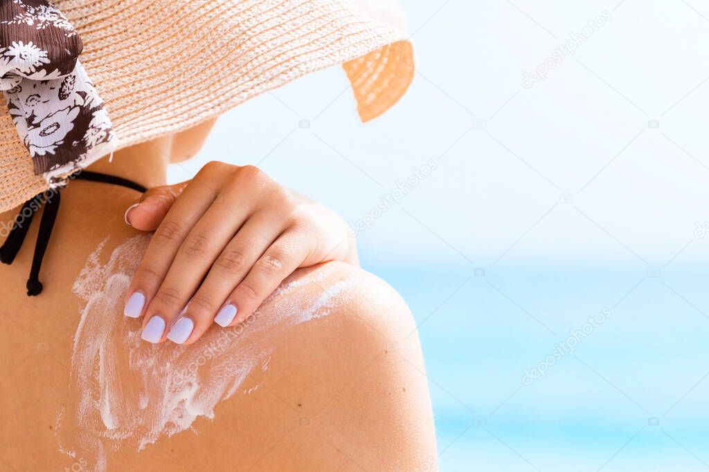 Sunscreen sunblock. Woman in a hat putting solar cream on shoulder outdoors under sunshine on beautiful summer day.