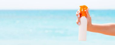 Denizin arka planında elinde güneş kremi tutan bir kadın resmi var..