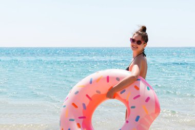 Güzel bir kadın plajda plajda plastik donut yüzüğüyle oynuyor..