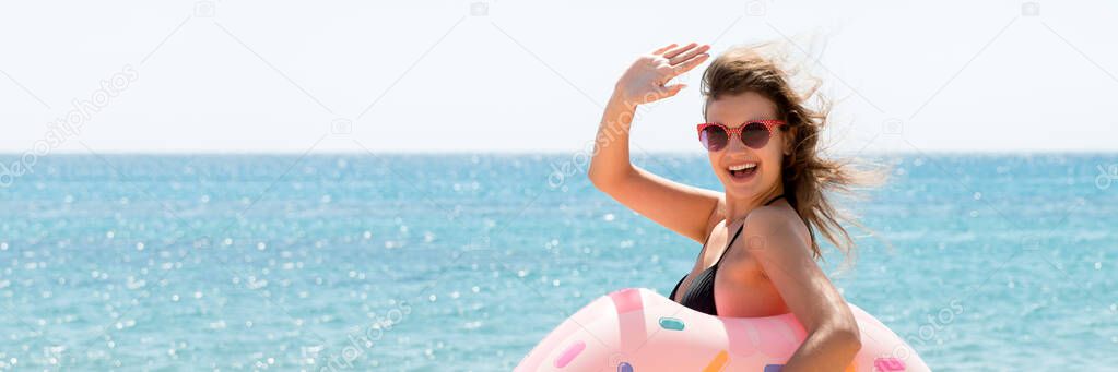 Portrait of young woman holding donut rubber ring and waving her hand at the sea background. Hot summer.