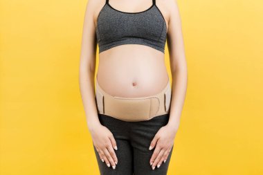 Hamile kadının sırtındaki ağrıyı azaltmak için arka planda fotokopi çekilen hamilelik kemeri görüntüsü. Ortopedik abdominal destek kemeri kavramı.