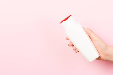 Kadın eli, pembe arka planda kozmetik şişesini tutuyor ve tasarımınız için boş bir alan yaratıyor..