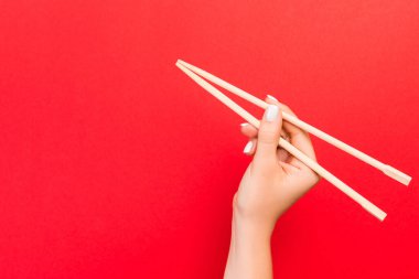 Kadının eli kırmızı arka planda yemek çubuklarını tutuyor. Tasarımınız için boş alanı olan Çin yemekleri konsepti.