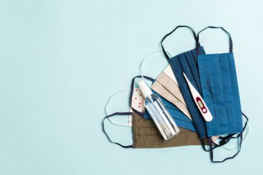 El yapımı pamuk maskeler, dijital termometre ve mavi arka planda alkol jeli dezenfektanı. Kopya alanı ile koruyucu ekipman kavramı.