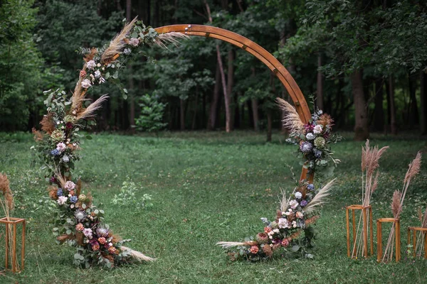 Arco redondo de boda en estilo rústico decorado con una composición de flores frescas para una ceremonia de boda al aire libre. Decoración rústica de moda . Imágenes de stock libres de derechos