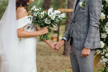 Gelin ve damat el ele tutuşuyor ve gelin beyaz çiçek buketi tutuyor. Düğün töreni..