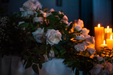 Karanlıkta bir masada beyaz gül ve yanan mumlar akşam yemeği için bir şenlik masası süslemesi, metin için yer.