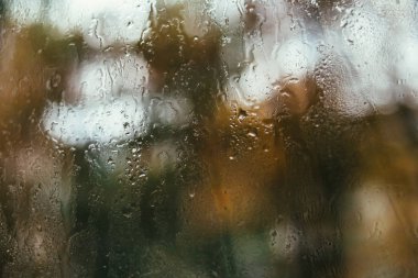 Caddenin bulanık yansıması sisli bir pencerede, bardaktan süzülen yağmur damlaları. Pencereye su damlıyor. Yağmurlu ruh hali.