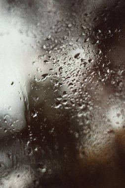 Caddenin bulanık yansıması sisli bir pencerede, bardaktan süzülen yağmur damlaları. Pencereye su damlıyor. Yağmurlu ruh hali.