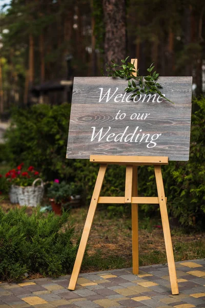 Placa de madeira com a inscrição Bem-vindo ao nosso casamento decorado com ramos verdes. Cerimônia de casamento . — Fotografia de Stock