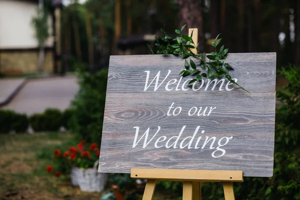 Placa de madeira com a inscrição Bem-vindo ao nosso casamento decorado com ramos verdes. Cerimônia de casamento . — Fotografia de Stock