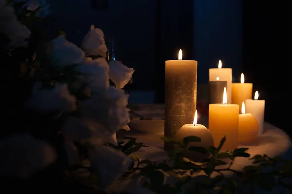 White rose and burning candles on a table in the dark, decoration of a festive table for dinner, space for text.