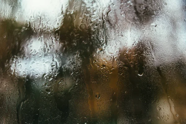 Blurred reflection of the street in a misted window, drops of water after rain flow down the glass. Water drops on window. Rainy mood concept.