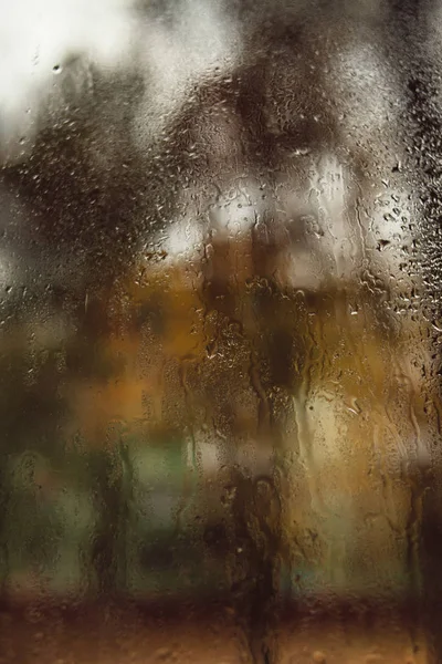 Blurred reflection of the street in a misted window, drops of water after rain flow down the glass. Water drops on window. Rainy mood concept.