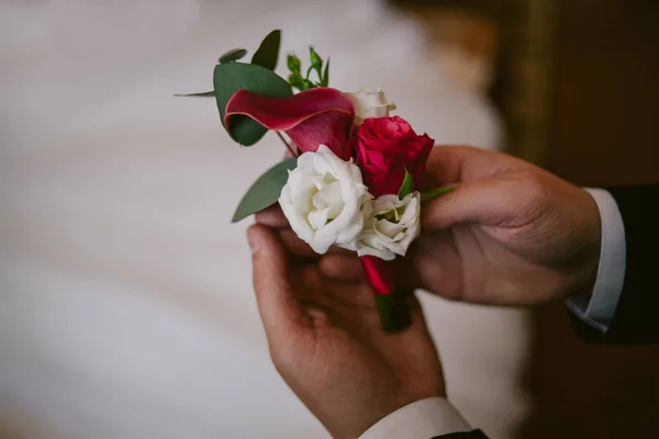 O noivo está segurando um belo casamento boutonniere contra o fundo de um vestido de noiva branco. Boutonniere close-up — Fotografia de Stock