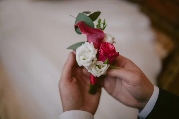 O noivo está segurando um belo casamento boutonniere contra o fundo de um vestido de noiva branco. Boutonniere close-up — Fotografia de Stock