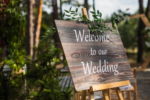 Tablero de madera con la inscripción Bienvenido a nuestra boda decorada con ramas verdes. Ceremonia de boda . Imagen de stock