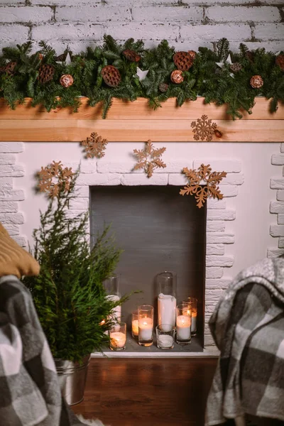 Decoratieve open haard versierd met Nieuwjaarsbloemenslinger en brandende kaarsen in glazen bekers. Gezellige kerstsfeer. — Stockfoto
