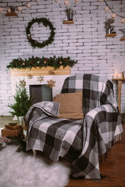 Fauteuil recouvert d'une couverture confortable, debout près de la cheminée décorée d'une guirlande de Noël . — Photo