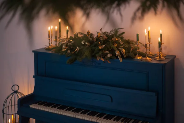 Um velho piano de cor azul, decorado com uma longa guirlanda de Natal de ramos de abeto e velas acesas para celebrar o feriado. Elementos dourados de decoração festiva. Conceito de férias de inverno . — Fotografia de Stock