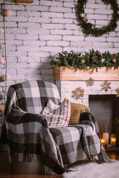 Sillón cubierto con una manta acogedora, de pie cerca de la chimenea decorada con una guirnalda de Navidad . Imagen de archivo