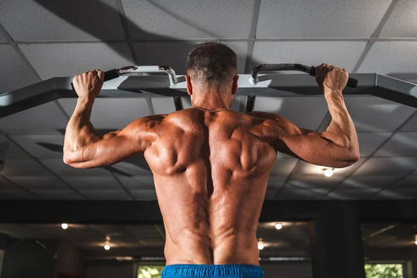 Idrottaren tränar ryggmusklerna på en vågrät stång med ett brett grepp. Lektioner i gymmet, hälsosam livsstil. — Stockfoto