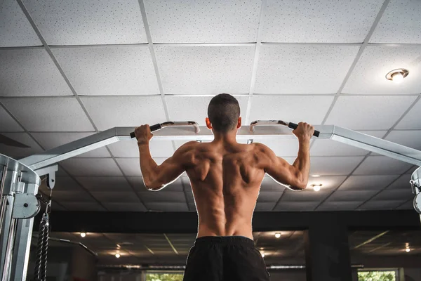 En ung idrottare tränar sina ryggmuskler på en vågrät stång med ett brett grepp. Lektioner i gymmet, hälsosam livsstil. — Stockfoto