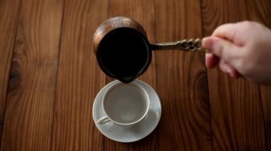 Barista bir fincana kahve doldurur. Tahta masanın üstünde dumanı tüten bir fincan Türk kahvesi, yukarıdan manzara. Kahve molası.