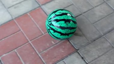 Eğimli bir yüzeyde yuvarlanan karpuza benzeyen bir top. Karpuz desenli çocuk balosu..