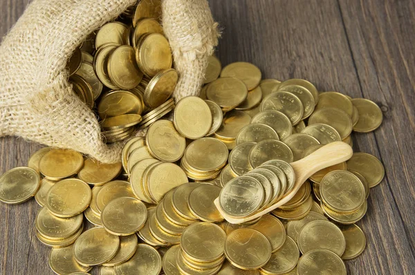 Gold coins in wood spoon with brown sack of coins — Stock Photo, Image