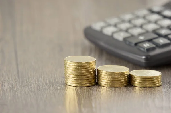 Primer plano paso monedas de oro han difuminado calculadora madera fondo —  Fotos de Stock