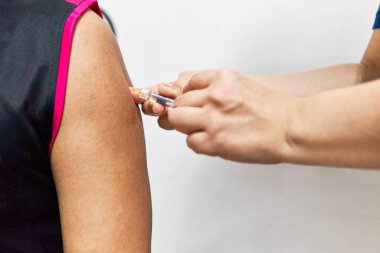 Elinde şırınga tutan hemşire, grip aşısını siyah kolsuz spor gömlekli bir adamın sol omzuyla enjekte ediyor. Adamın omzunu kapat. Sağlık ve sağlık konsepti fotoğrafçılığı.