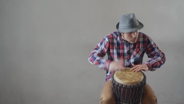 Un hombre gracioso con bigote y sombrero tocando el tambor étnico. Músico caucásico tocando el tambor étnico. Hipster hombre tocando música étnica en el tom-tom. Copiar pasta — Vídeos de Stock