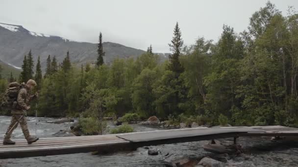 Resenären korsar träbron över den vackra bergsfloden i den natursköna skogen. Långsamma rörelser — Stockvideo