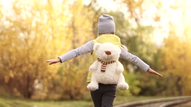 Achteraanzicht van klein eenzaam meisje wandelen op de spoorweg met Teddy beer — Stockvideo