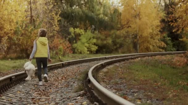 Одинокая маленькая девочка с плюшевым мишкой на плечах на железной дороге. — стоковое видео
