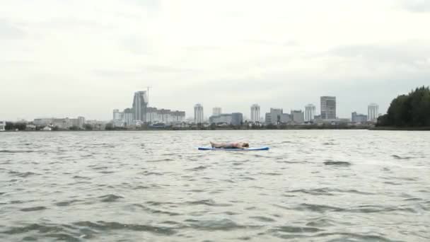 Jonge vrouw ontspannen op een sup Board. Stadsgezicht op de achtergrond. — Stockvideo