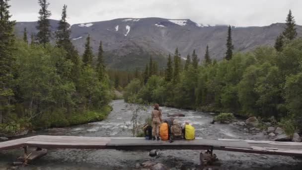 A group of travelers relax sitting on the bridge and admire the amazing view — 비디오