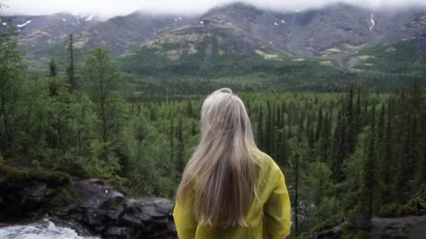 Vista posterior de la chica de pie sobre la roca y mirando al horizonte con montañas. Concepto de vacaciones, viajes y aventuras — Vídeos de Stock