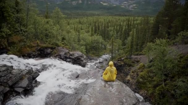 Sarı yağmurluklu bir adam uçuruma oturur ve meditasyon yapar. — Stok video