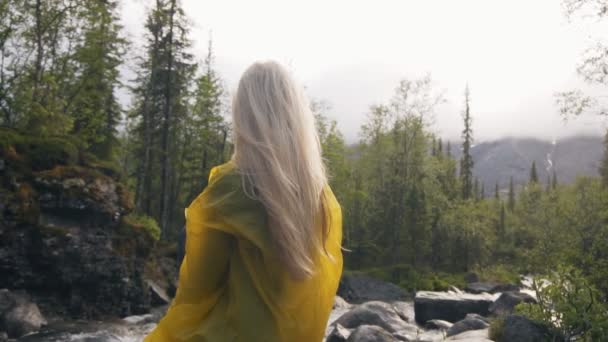 Una vista desde la parte posterior de una chica de viaje con el pelo largo y rubio se sienta en una montaña y admira la hermosa vista — Vídeos de Stock